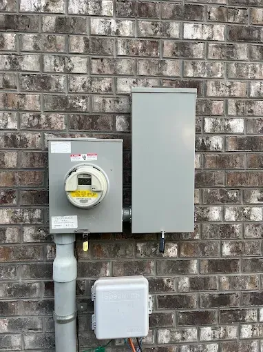 Electrical meter box and panel on a brick wall. Gray boxes, pipes, and wiring.