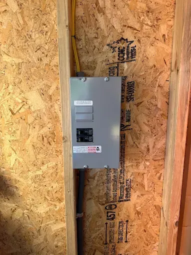 Gray electrical panel mounted on a wood-paneled wall, with conduit and wiring visible.