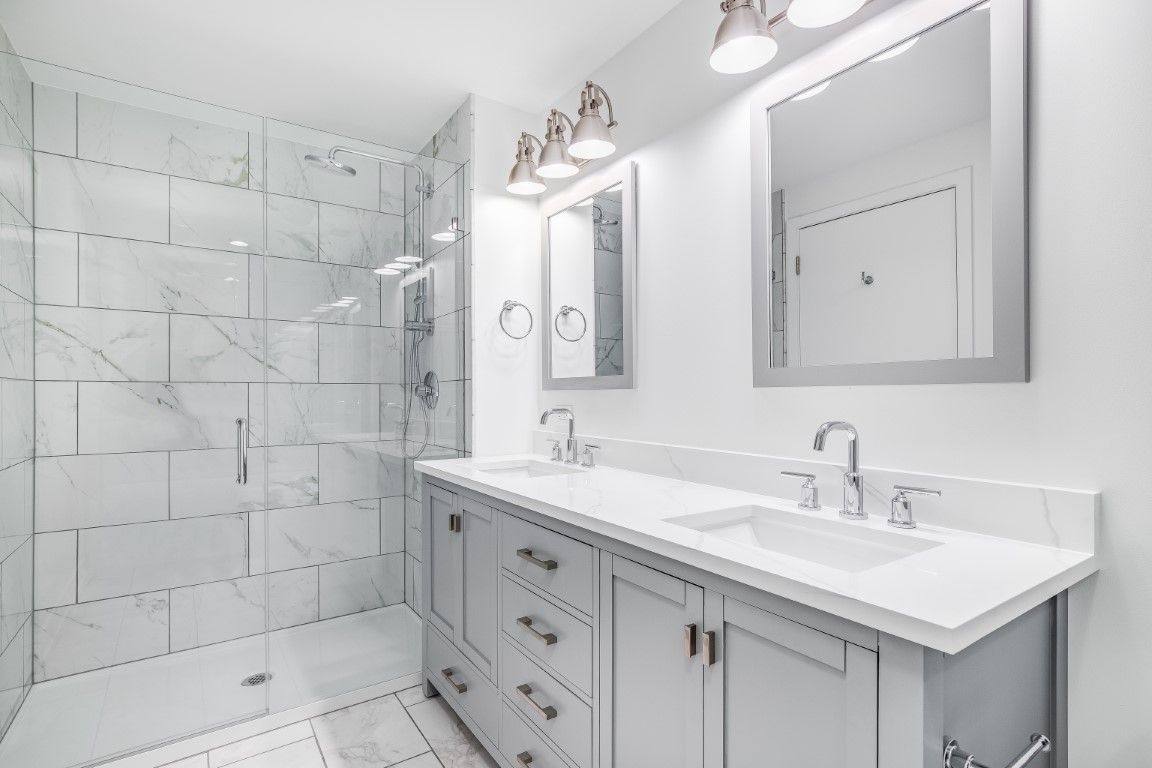Modern bathroom with white and gray marble tiles, double vanity, and glass shower.