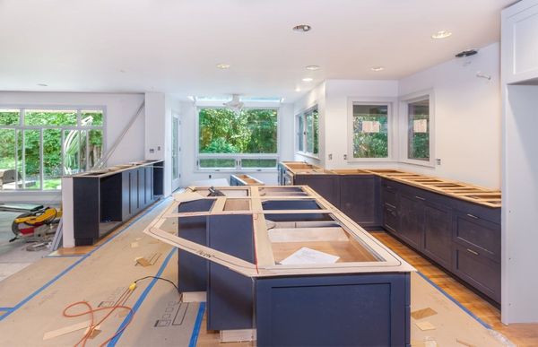 Kitchen remodel in progress: dark blue cabinets, unfinished countertops, large windows overlooking greenery.