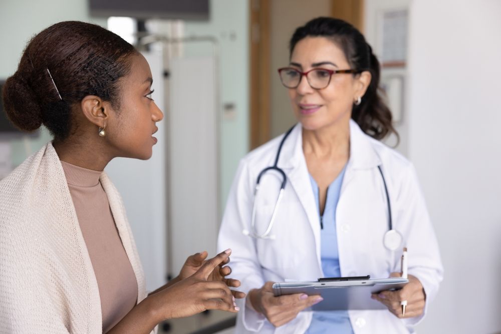 Woman talking with a doctor in a medical office; doctor holding a clipboard.