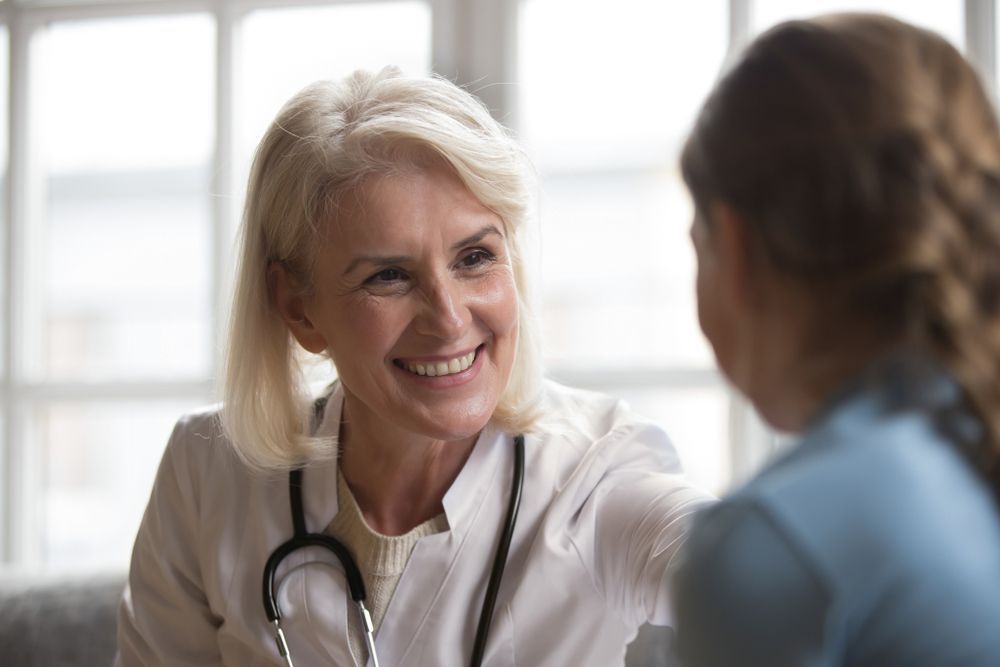 Doctor smiles and touches patient's shoulder indoors, stethoscope around neck.