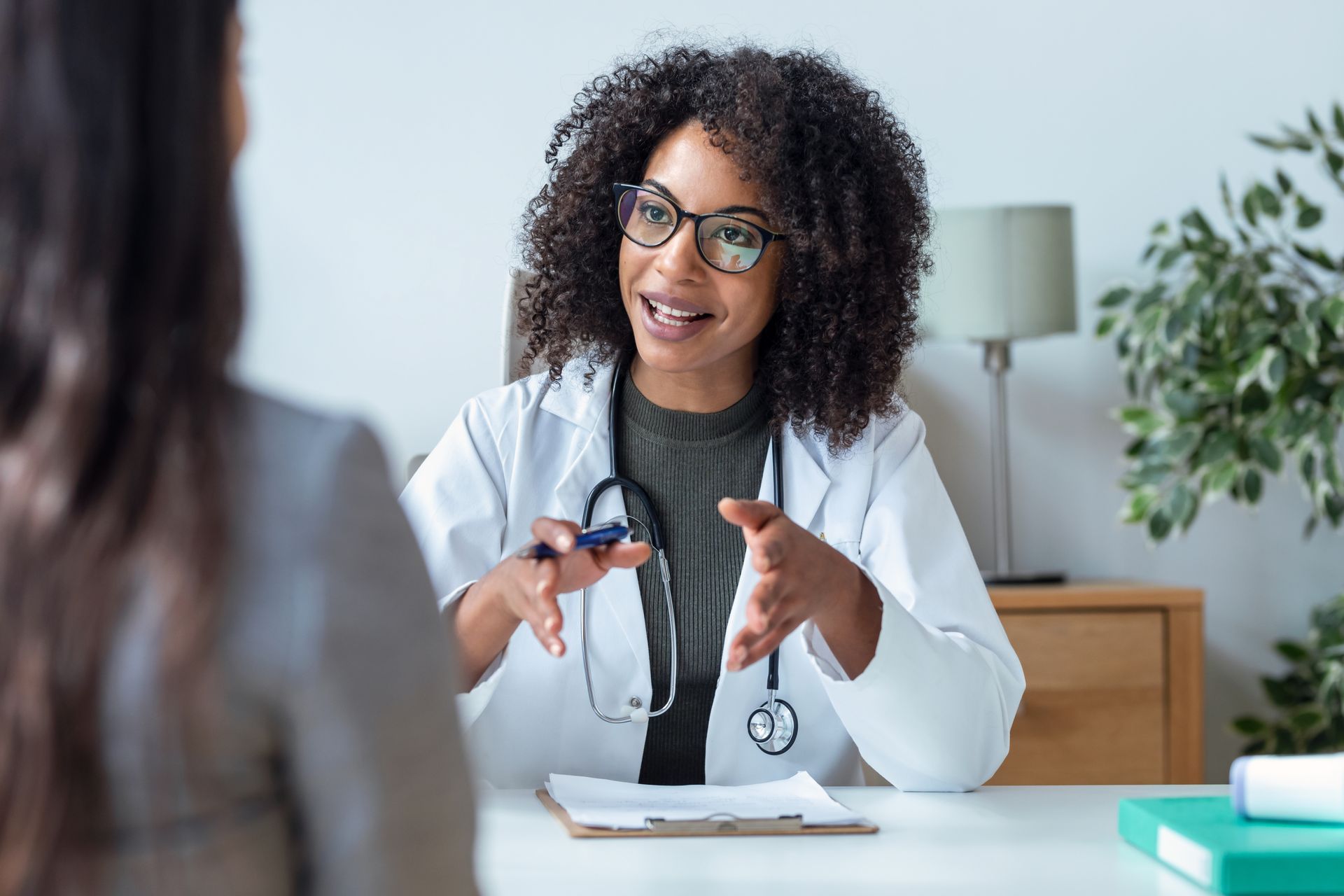 Doctor in white coat speaking with a patient at a desk, office setting.