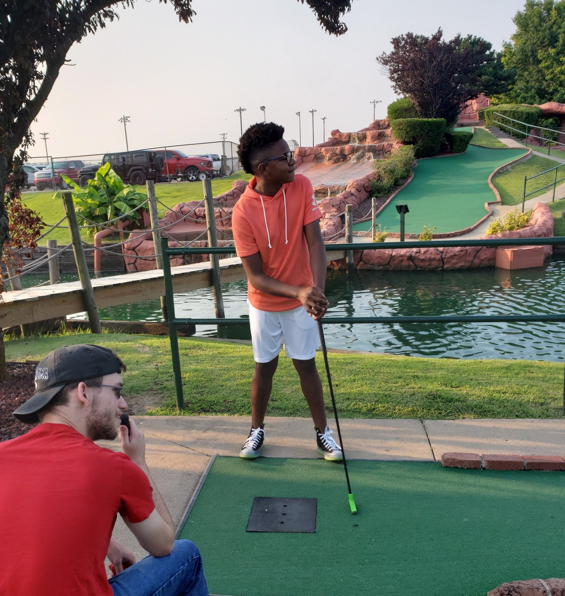 A young boy in an orange shirt is playing mini golf