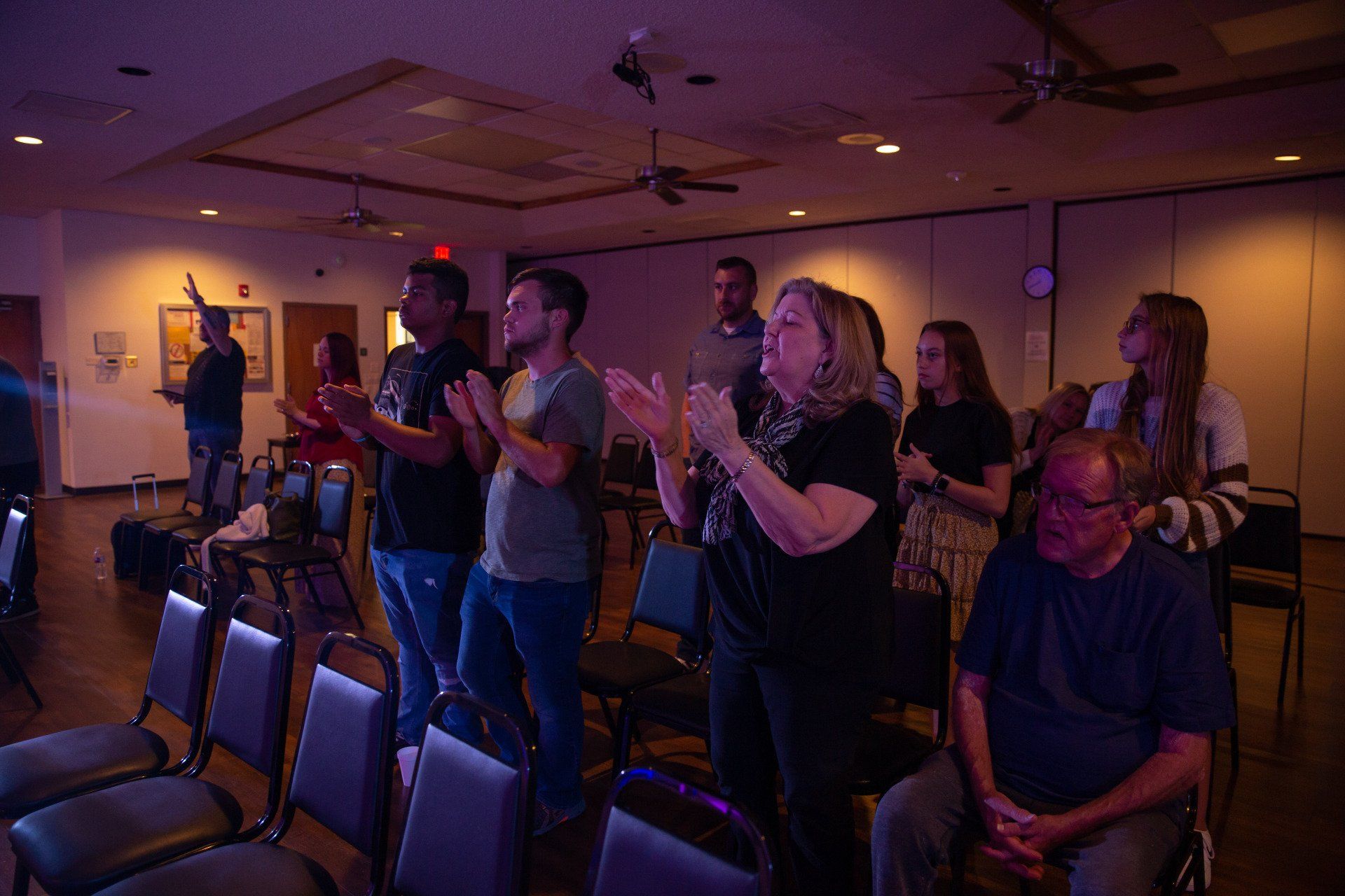 A group of people are standing in a room singing and applauding.