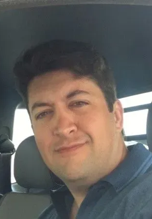 Uma mulher de camisa branca com os braços no bolço sorrindo para a câmera