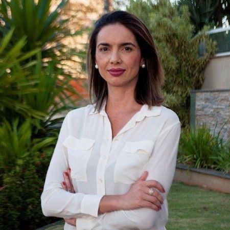 Uma mulher está sentada em um banquinho vestindo uma jaqueta preta e uma blusa vermelha.