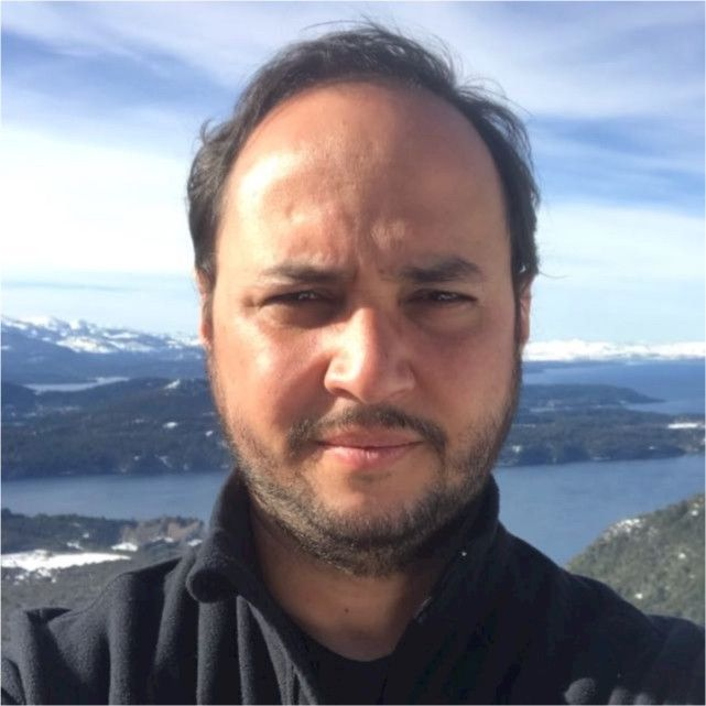 Um homem usando óculos e uma camisa azul sorri para a câmera