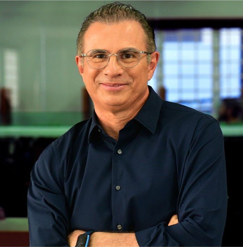 Um homem usando óculos e uma camisa azul sorri para a câmera