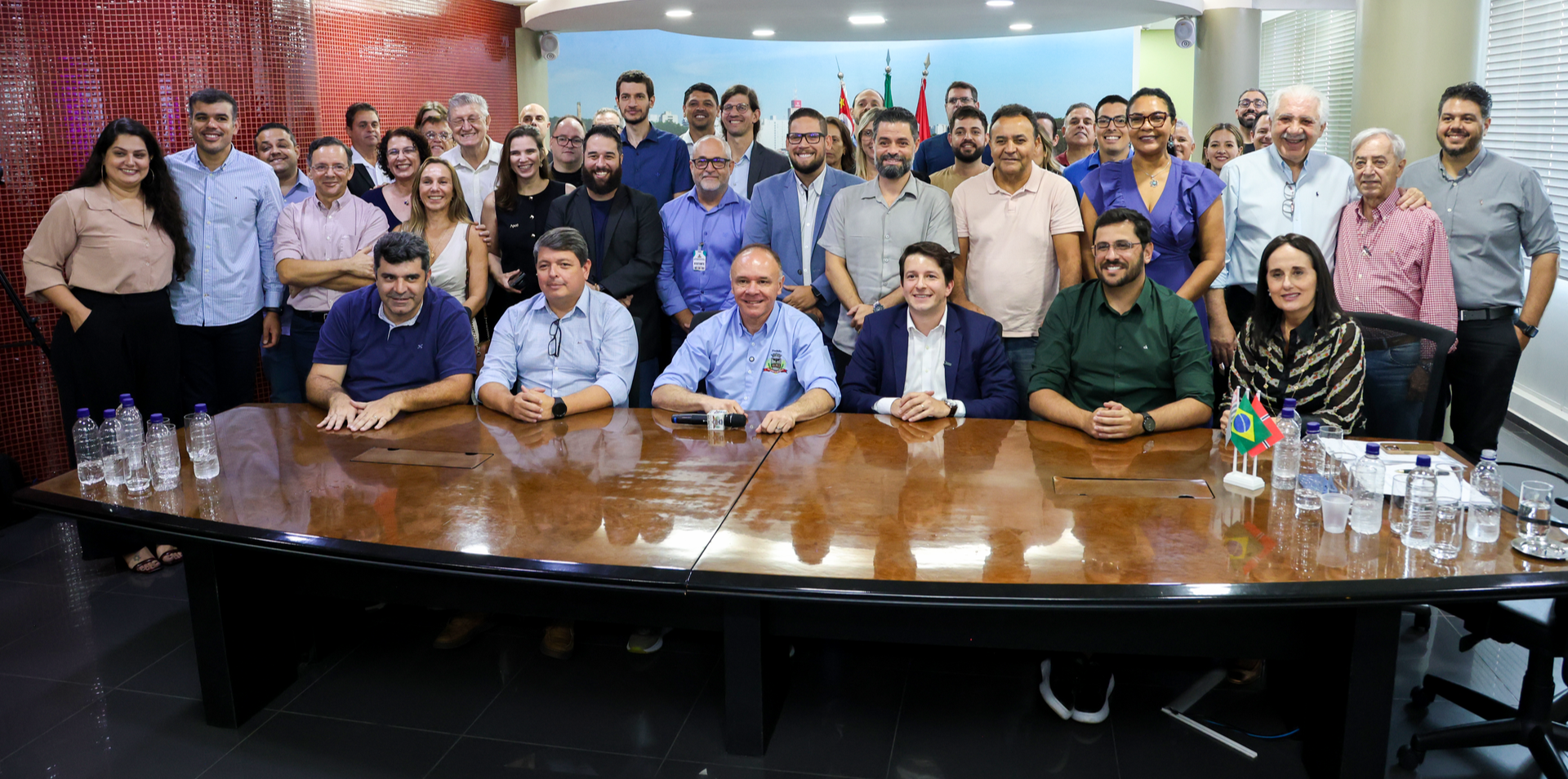 A group of people seated and standing around a large wooden boardroom table at a professional meeting.