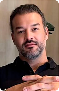 Um homem usando óculos e uma camisa azul sorri para a câmera