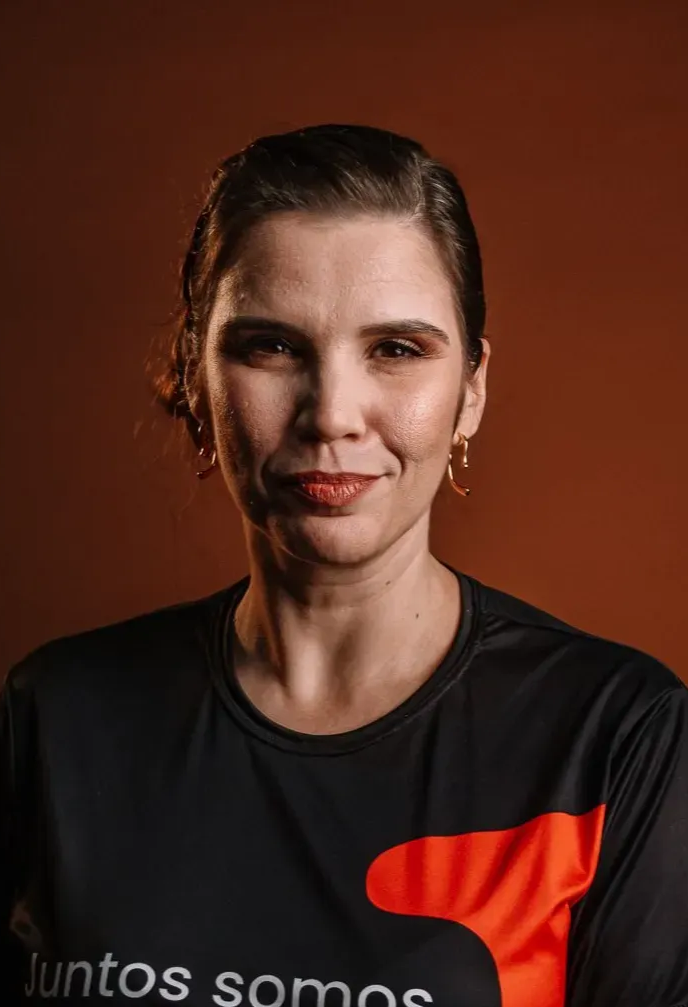 Uma mulher de camisa branca com os braços no bolço sorrindo para a câmera