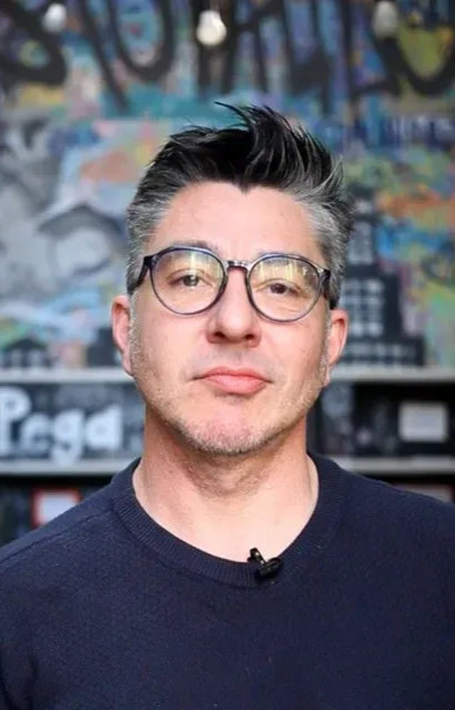 Um homem de terno e óculos está sorrindo para a câmera.