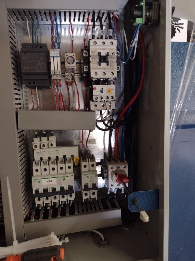 Open industrial electrical control panel with various wiring, breakers, contactors, and a red rotary power switch.