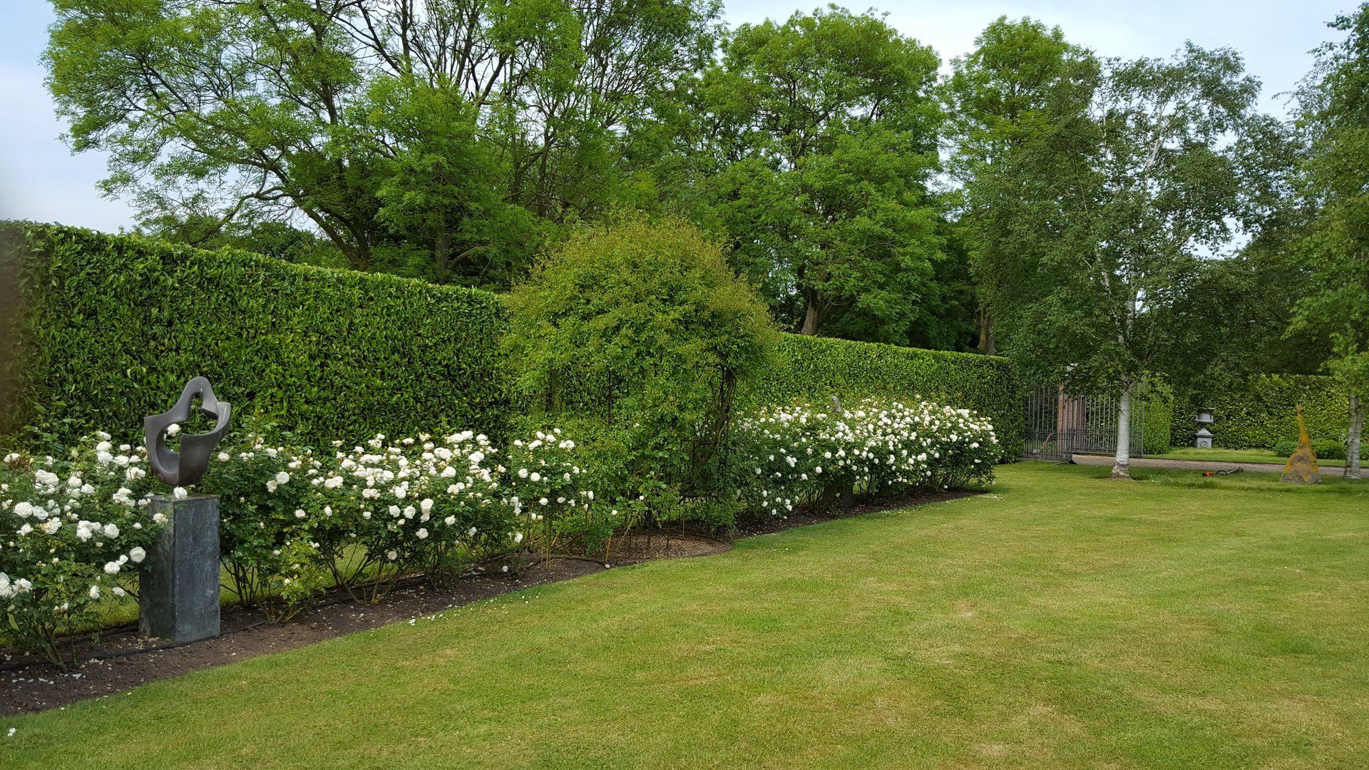 Neatly trimmed hedge behind white flowerbed and ornament