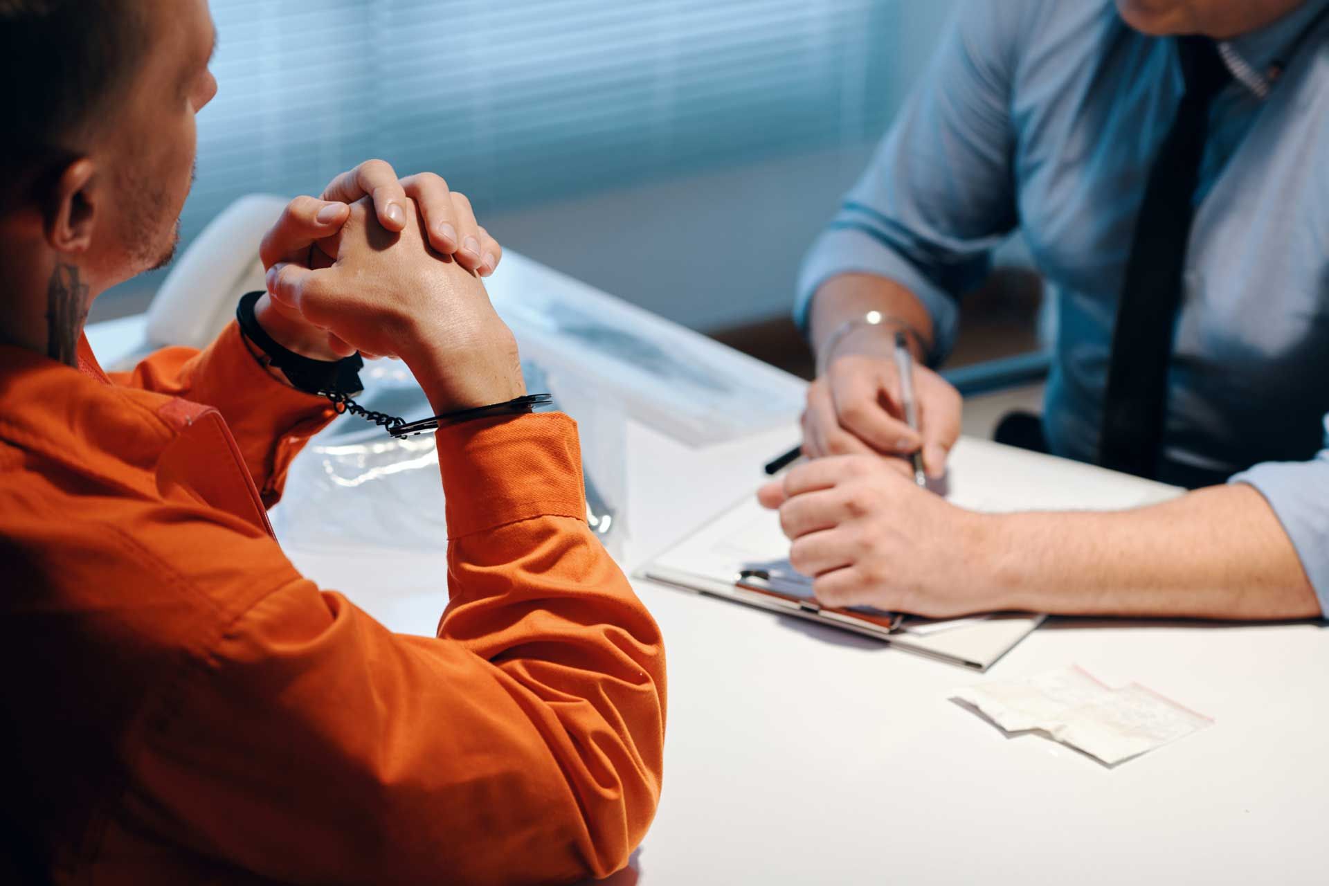 A man in handcuffs is sitting at a table with a man in a suit.