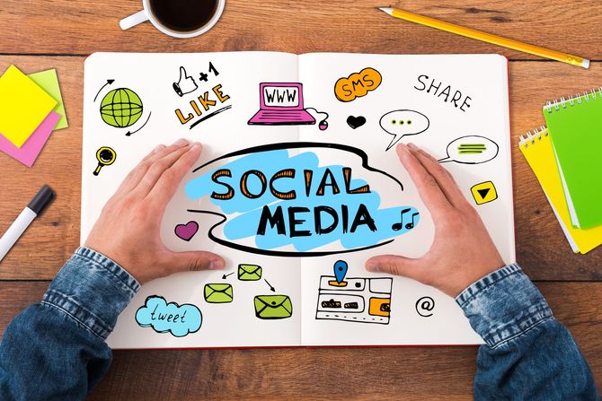 Hands framing a SOCIAL MEDIA sign with colorful icons on a desk