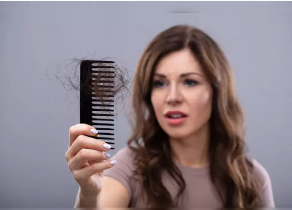 A woman is holding a comb with hair falling out of it.