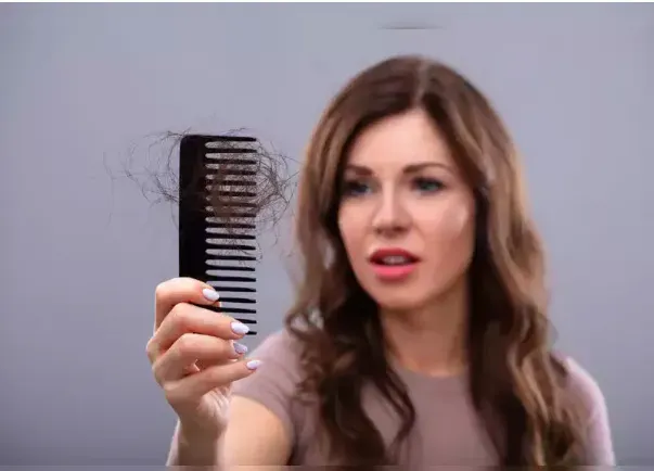 A woman is holding a comb with hair falling out of it.