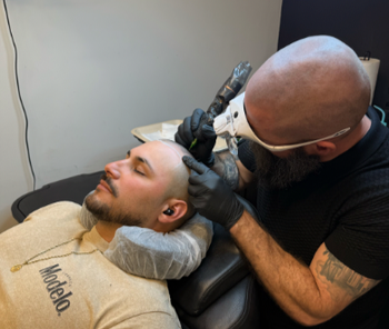 An SMP INK CDA Student Practitioner drawing the reference line on the scalp of  an SMP client in a class setting.