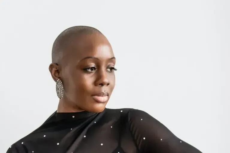 A woman with a shaved head is wearing a black dress and earrings.