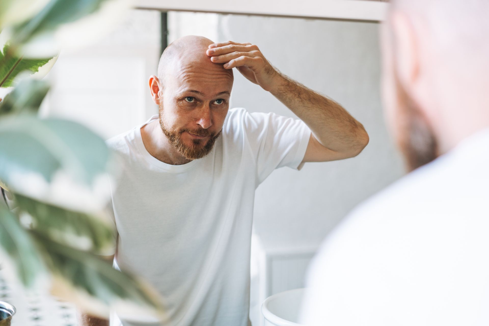 A bald man is looking at his hair in the mirror.