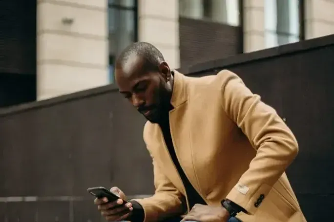 A man in a yellow jacket is looking at his cell phone.