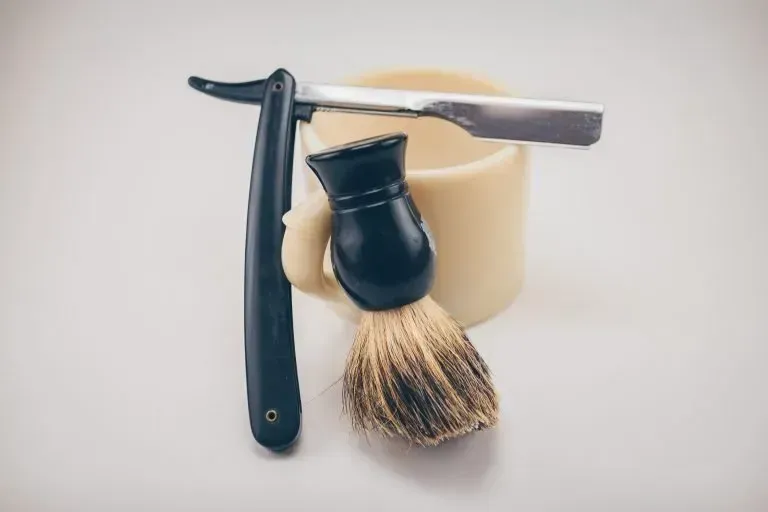 A razor and a shaving brush are sitting on top of a shaving mug.