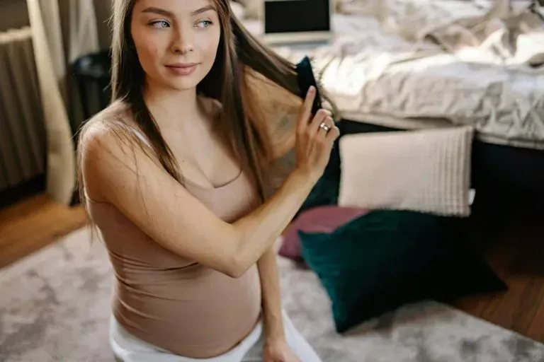 A pregnant woman is brushing her hair in a bedroom.