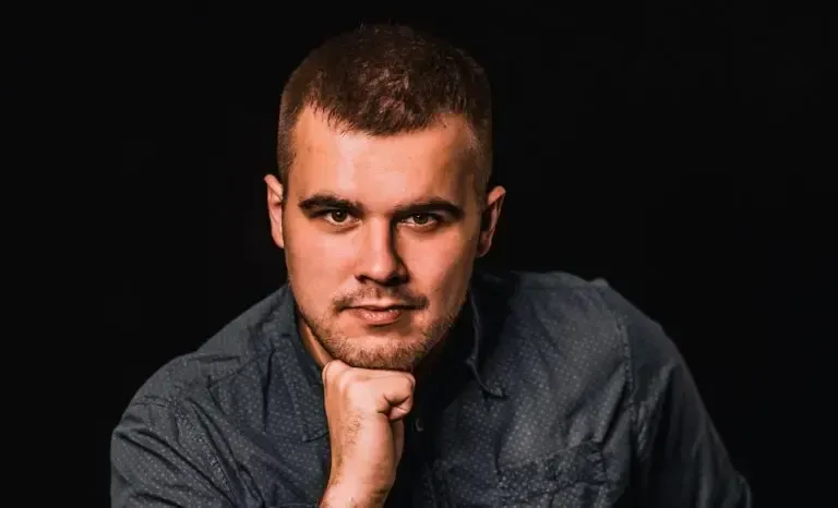 A man is holding his hand to his chin and looking at the camera.
