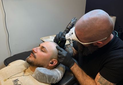 An SMP INK CDA Student Practitioner drawing the reference line on the scalp of  an SMP client in a class setting.