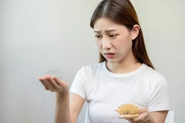 A woman is holding a brush in her hand and looking at her hair.