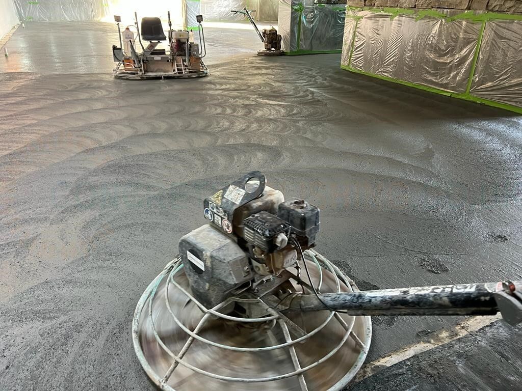 Concrete power trowels sitting on a newly poured gray concrete floor inside a building under construction.