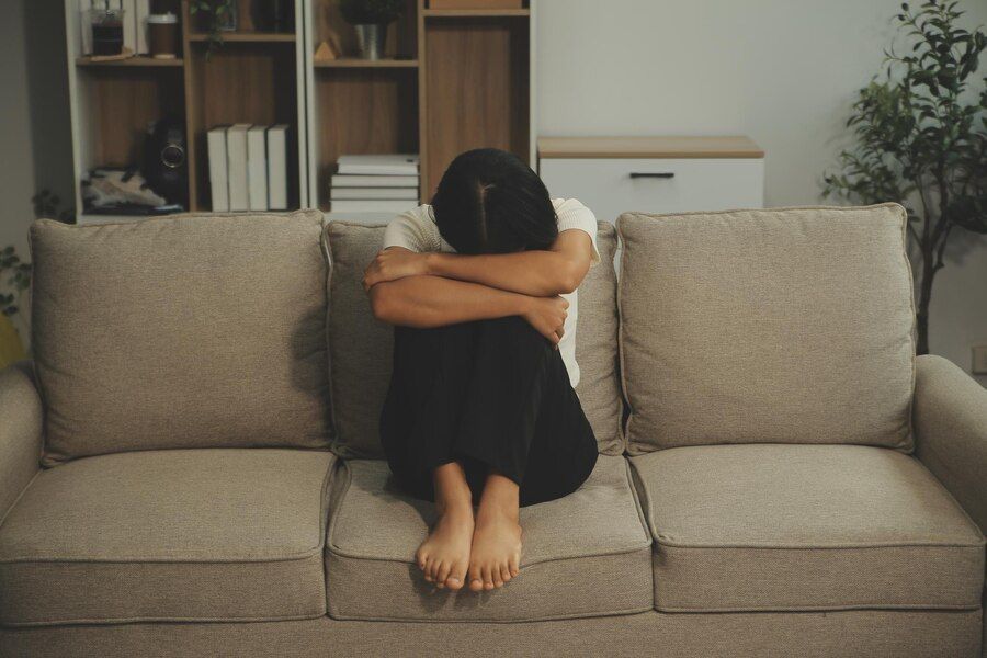 A woman is sitting on a couch with her head in her hands.