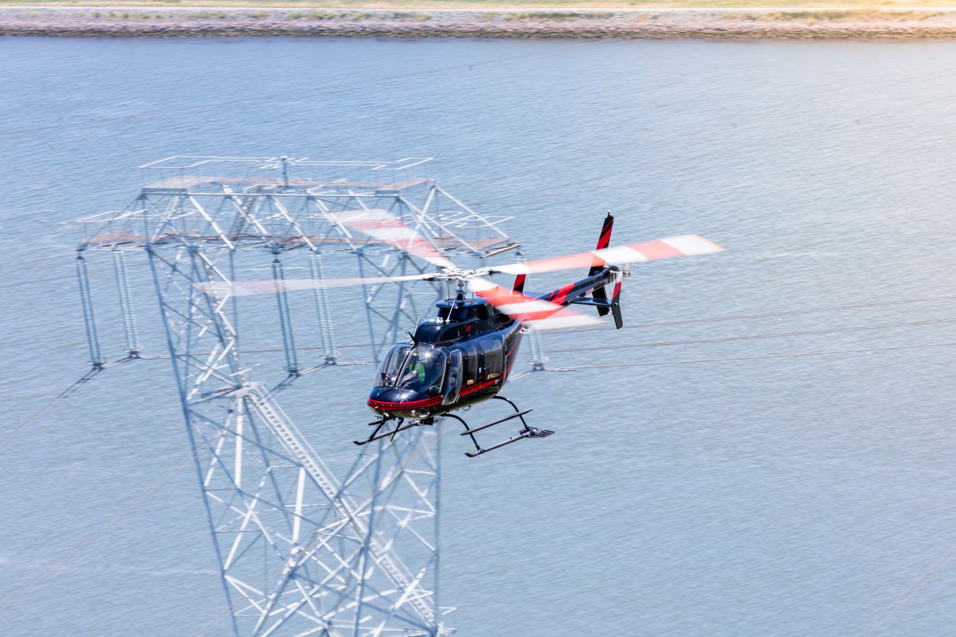 A helicopter is flying over a power tower in the water.