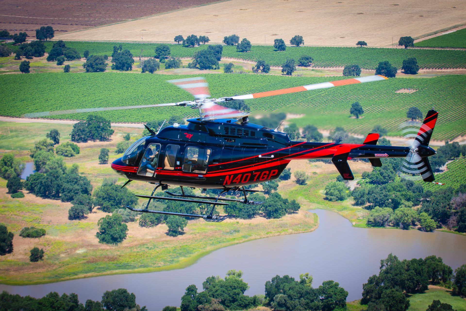 A red and black helicopter is flying over a body of water.