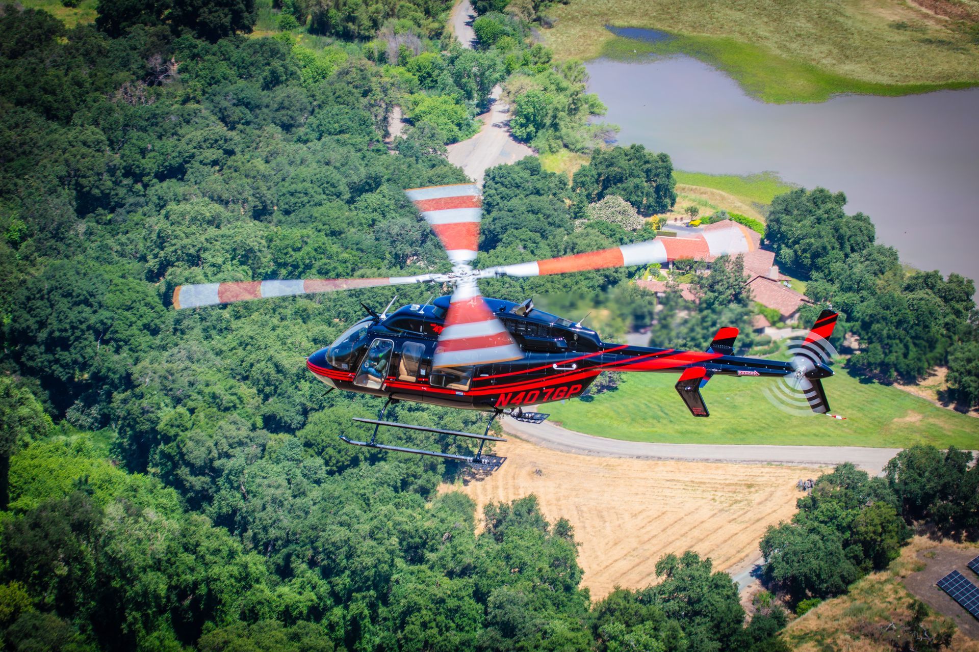 A red and white helicopter is flying over a lush green forest.