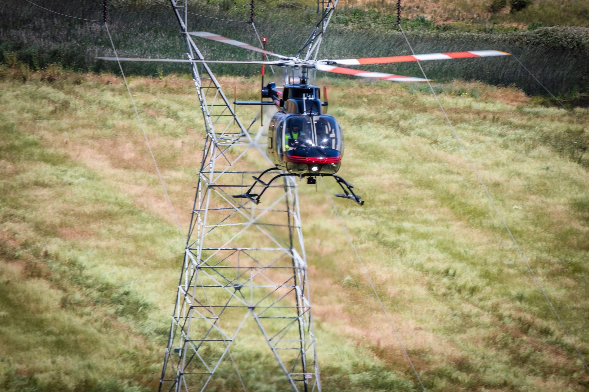 A helicopter is flying over a power line in a field.