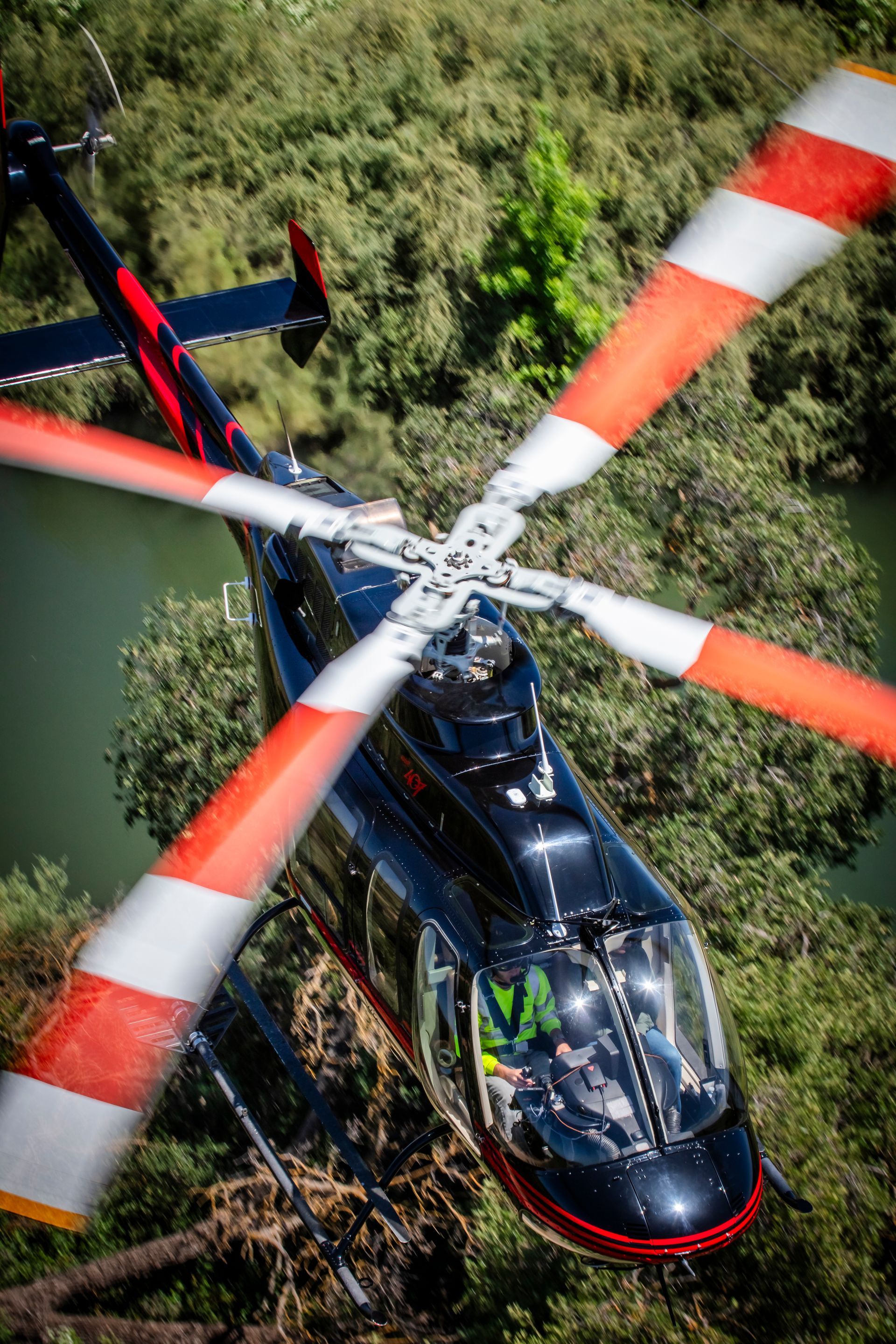 A helicopter is flying over a body of water surrounded by trees.