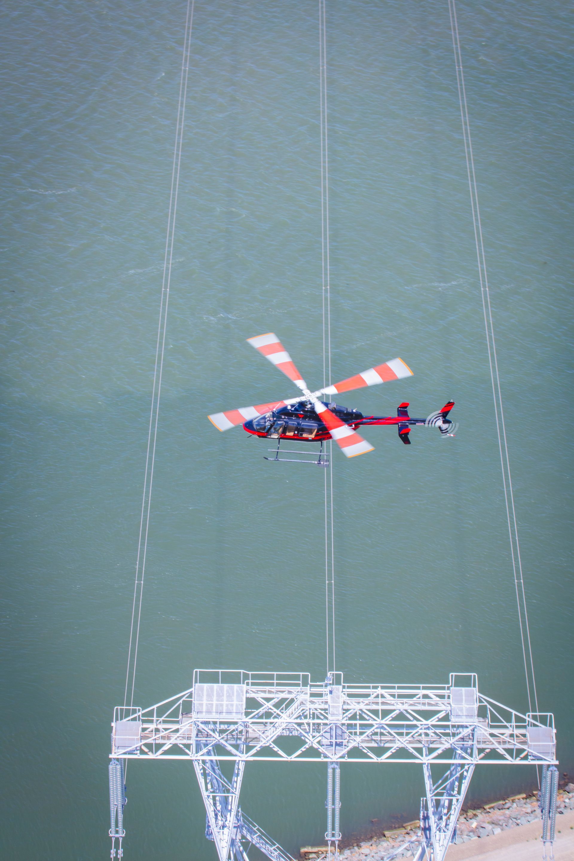A helicopter is flying over a power tower in the water.
