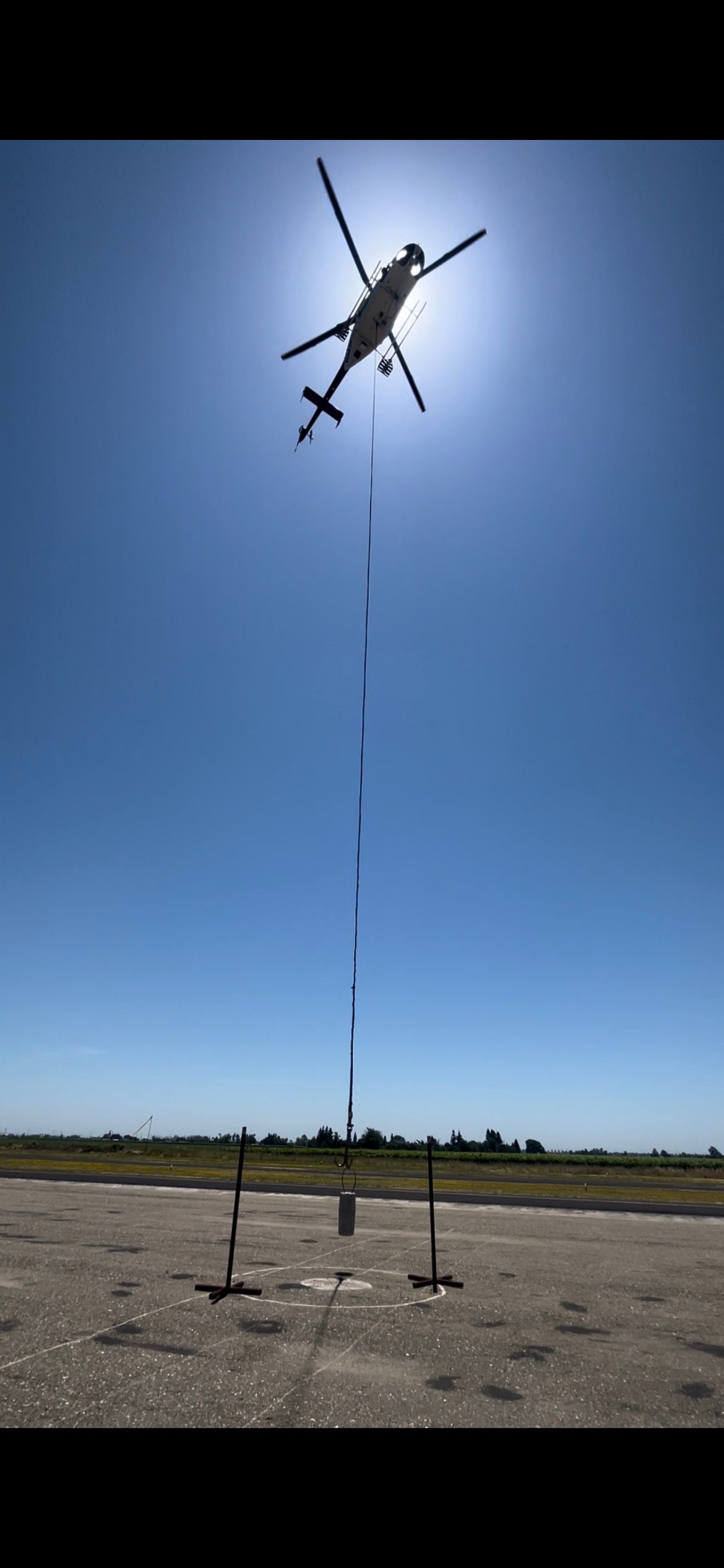 A helicopter is flying over a runway with the sun behind it