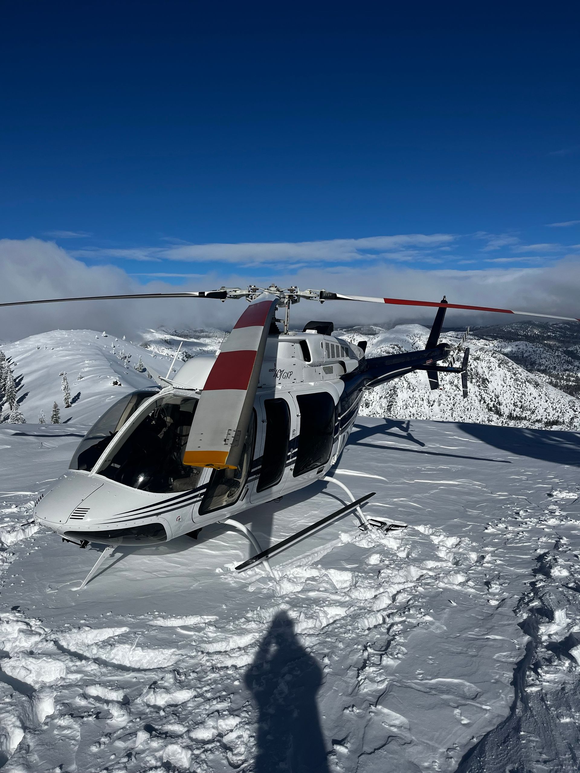 A helicopter is sitting on top of a snow covered mountain.