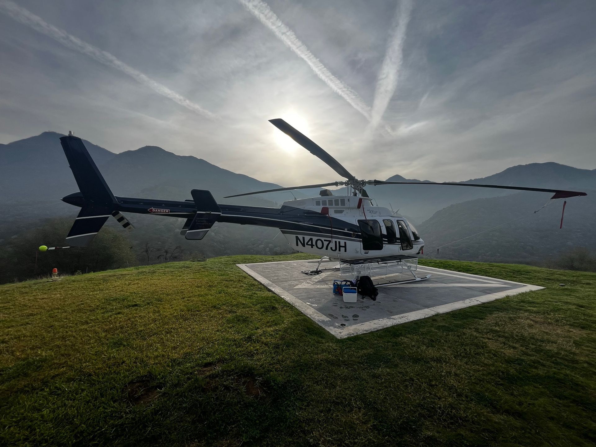 A helicopter is parked on a grassy hill with mountains in the background.