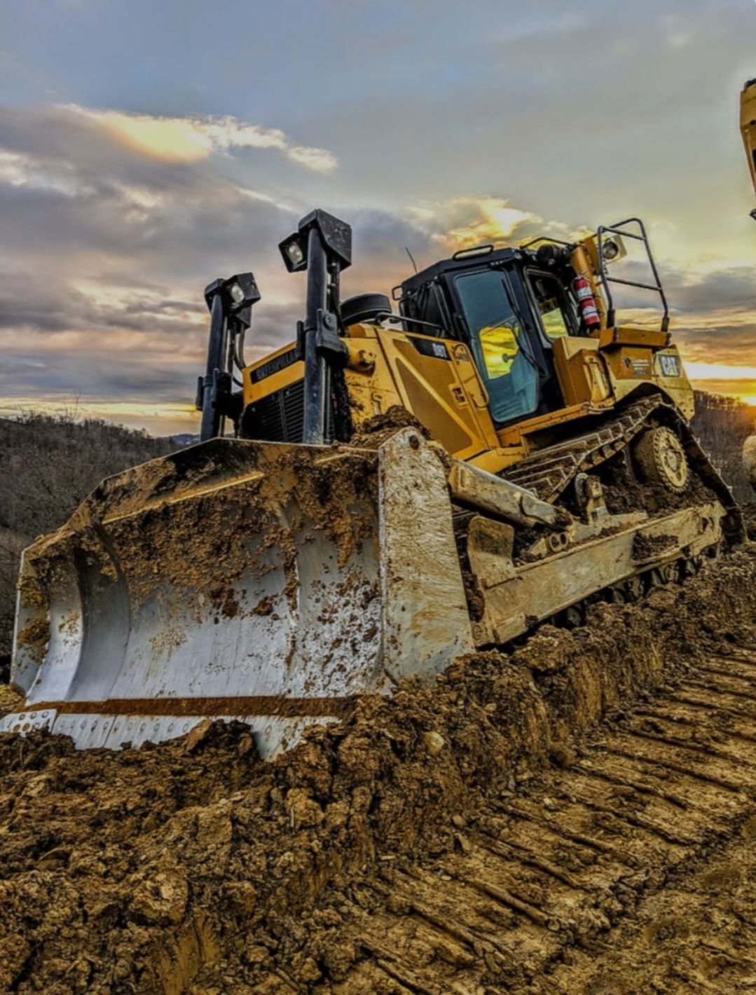 A bulldozer is driving through a dirt field at sunset.