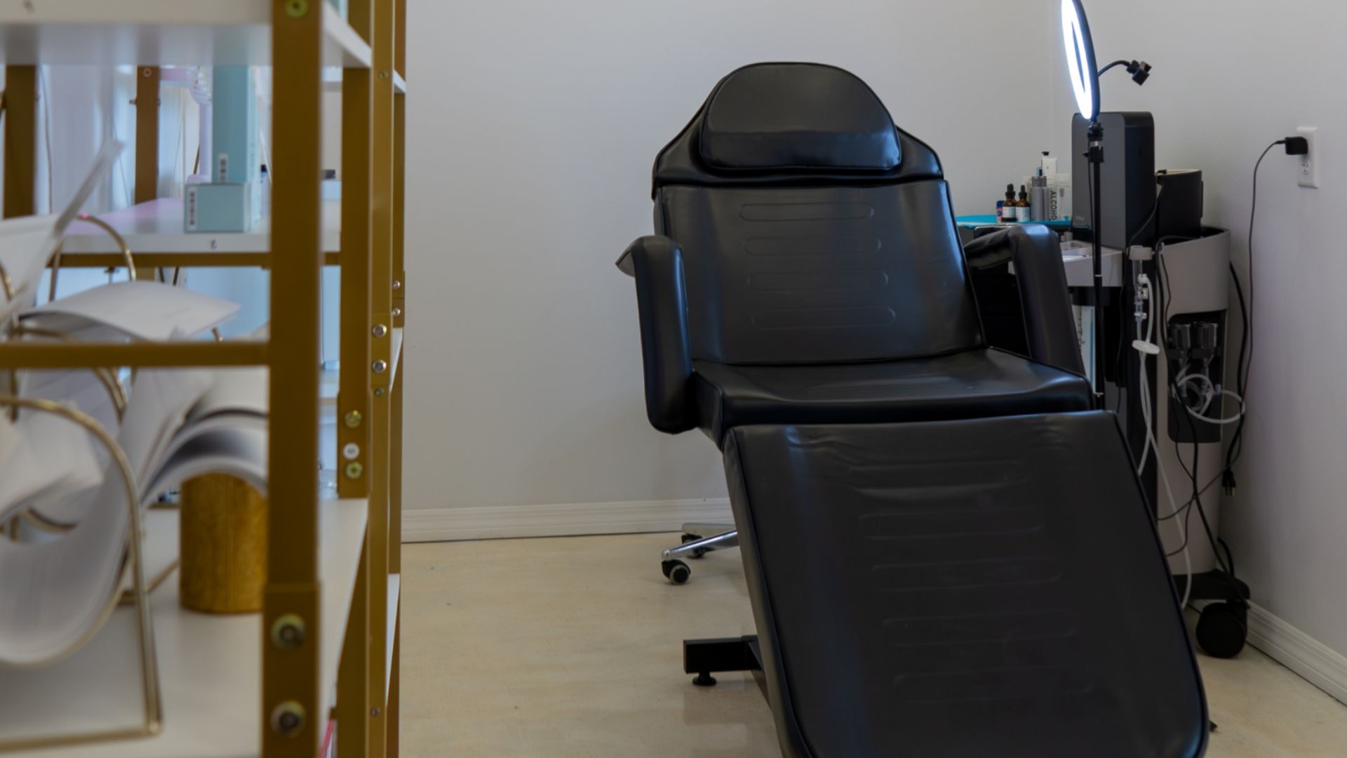 Black recliner chair in a clinical room beside medical equipment and a glass door