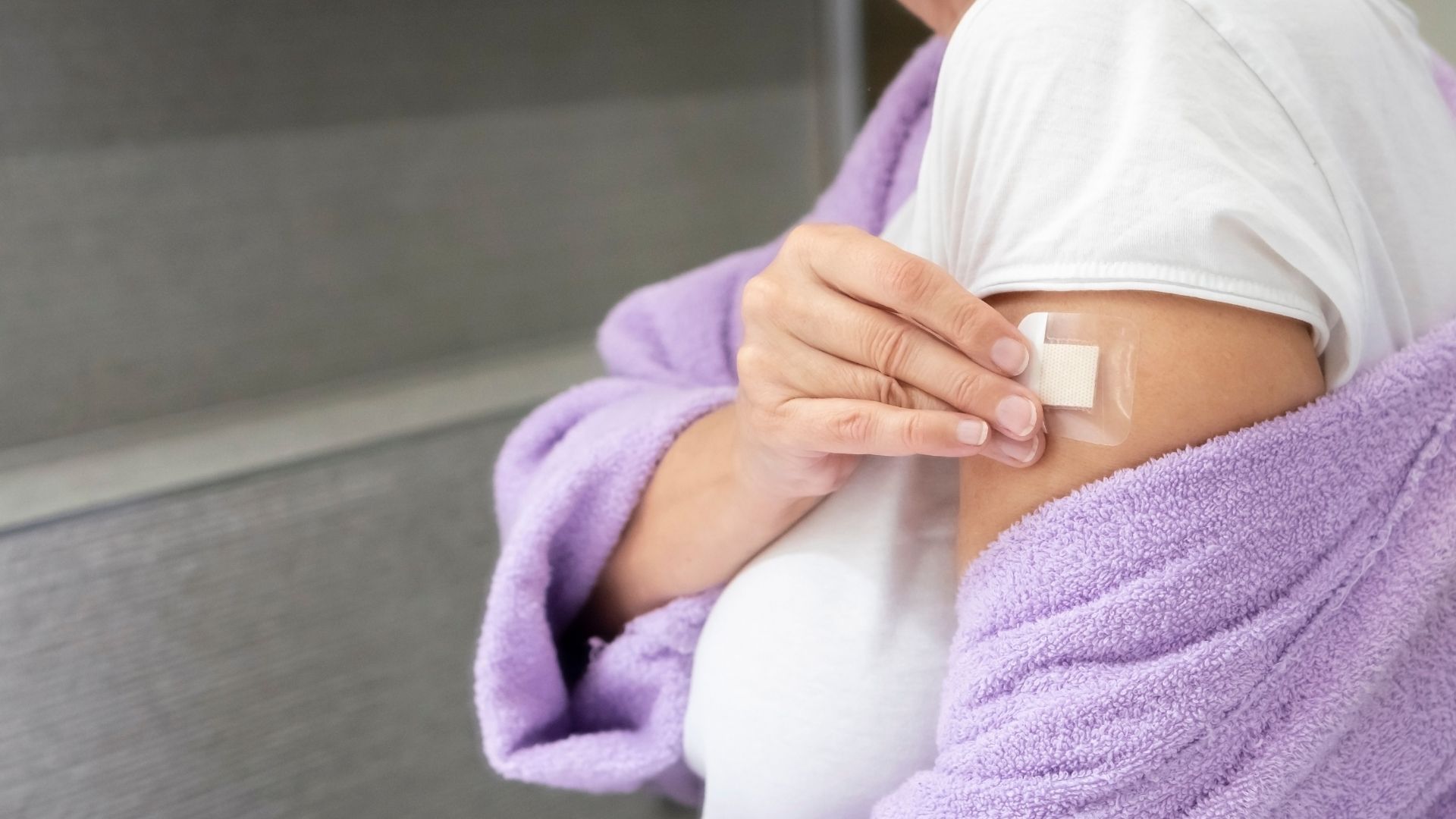 Person applying a clear adhesive bandage to an upper arm while wearing a purple robe