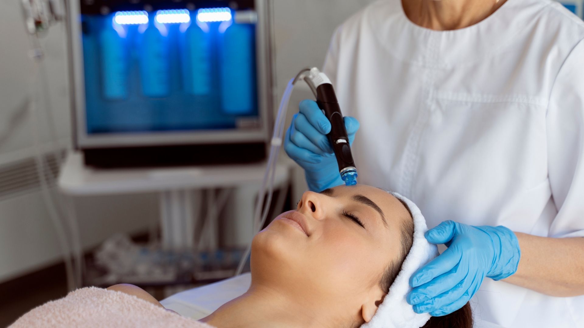 Esthetician applying a facial treatment with a handheld device to a reclining client in a spa setting