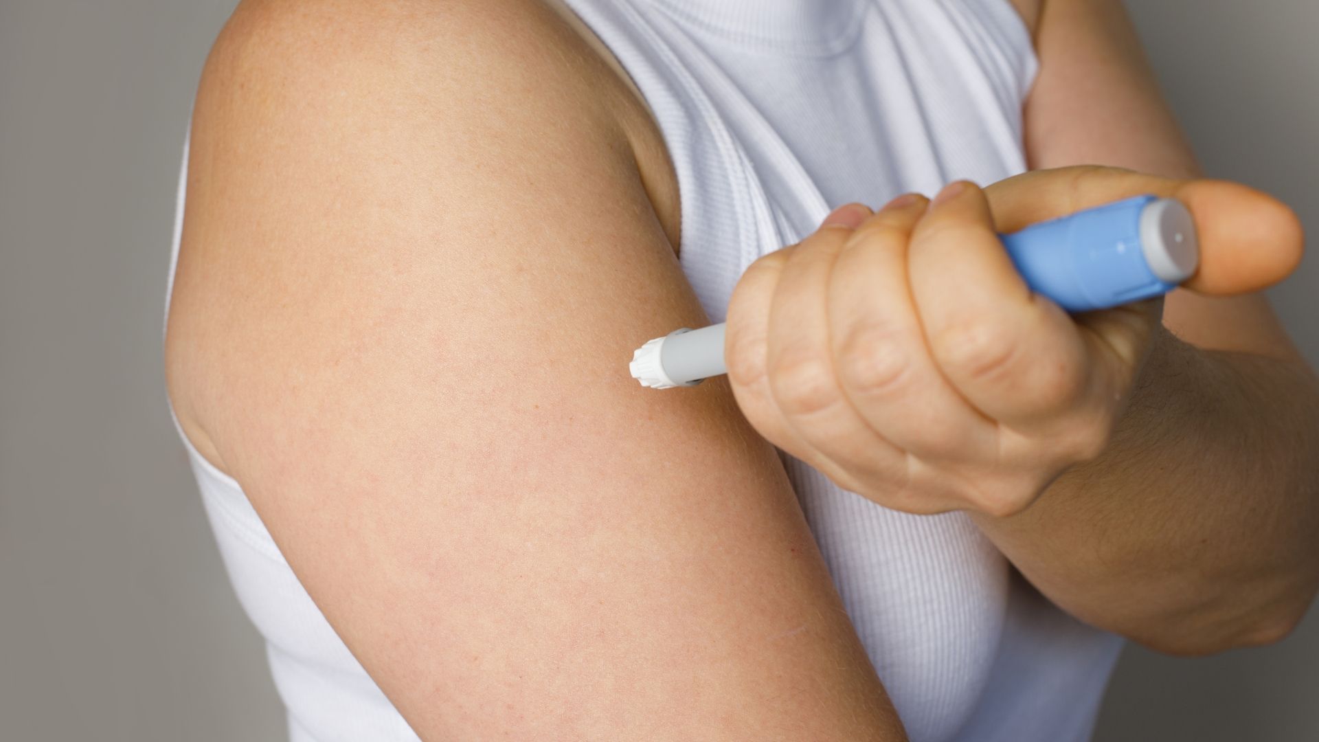 Person holding an injection pen near a bare upper arm, preparing to administer a shot