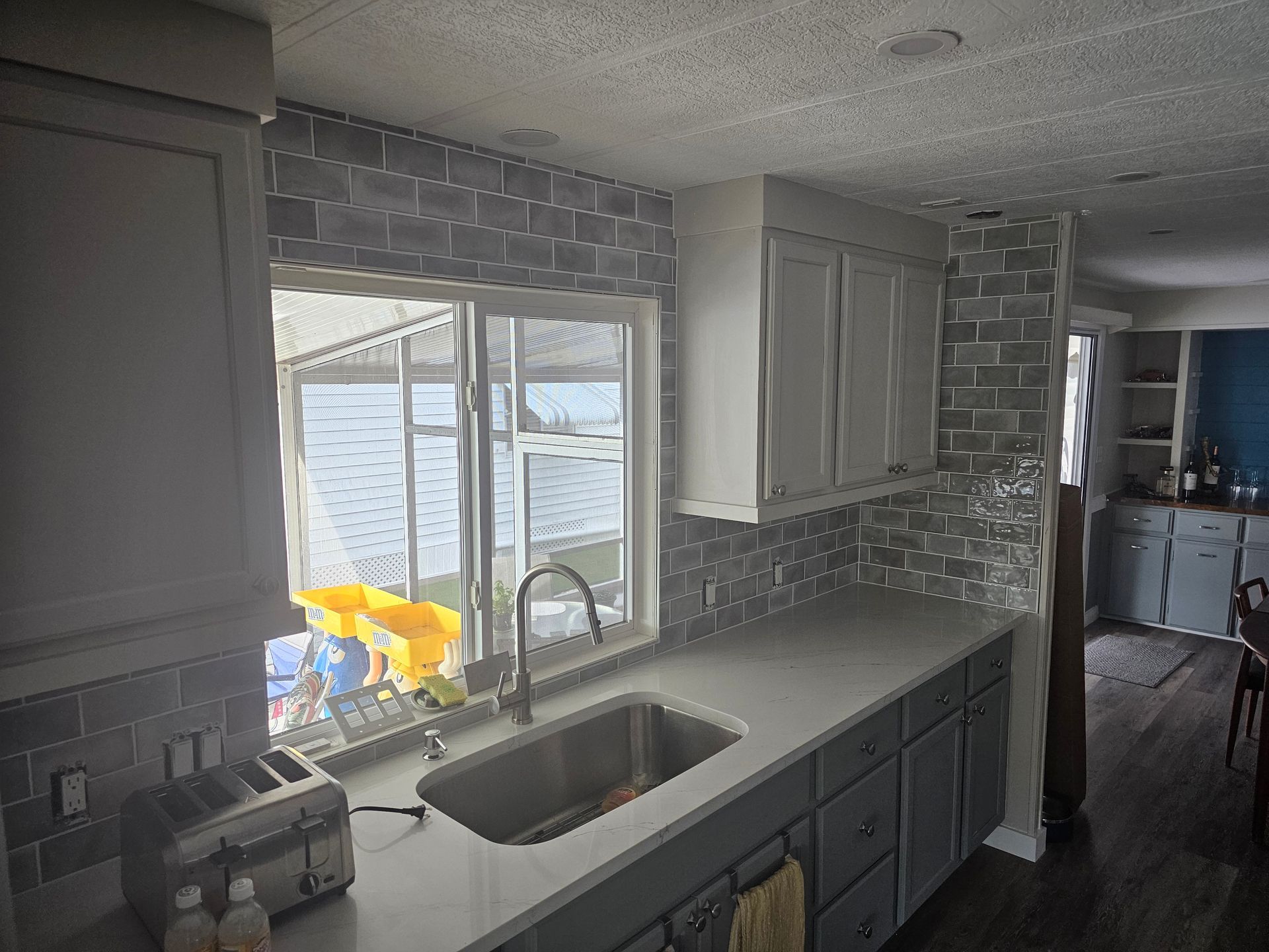 Gray and white kitchen with a window, sink, cabinets, and tiled backsplash.
