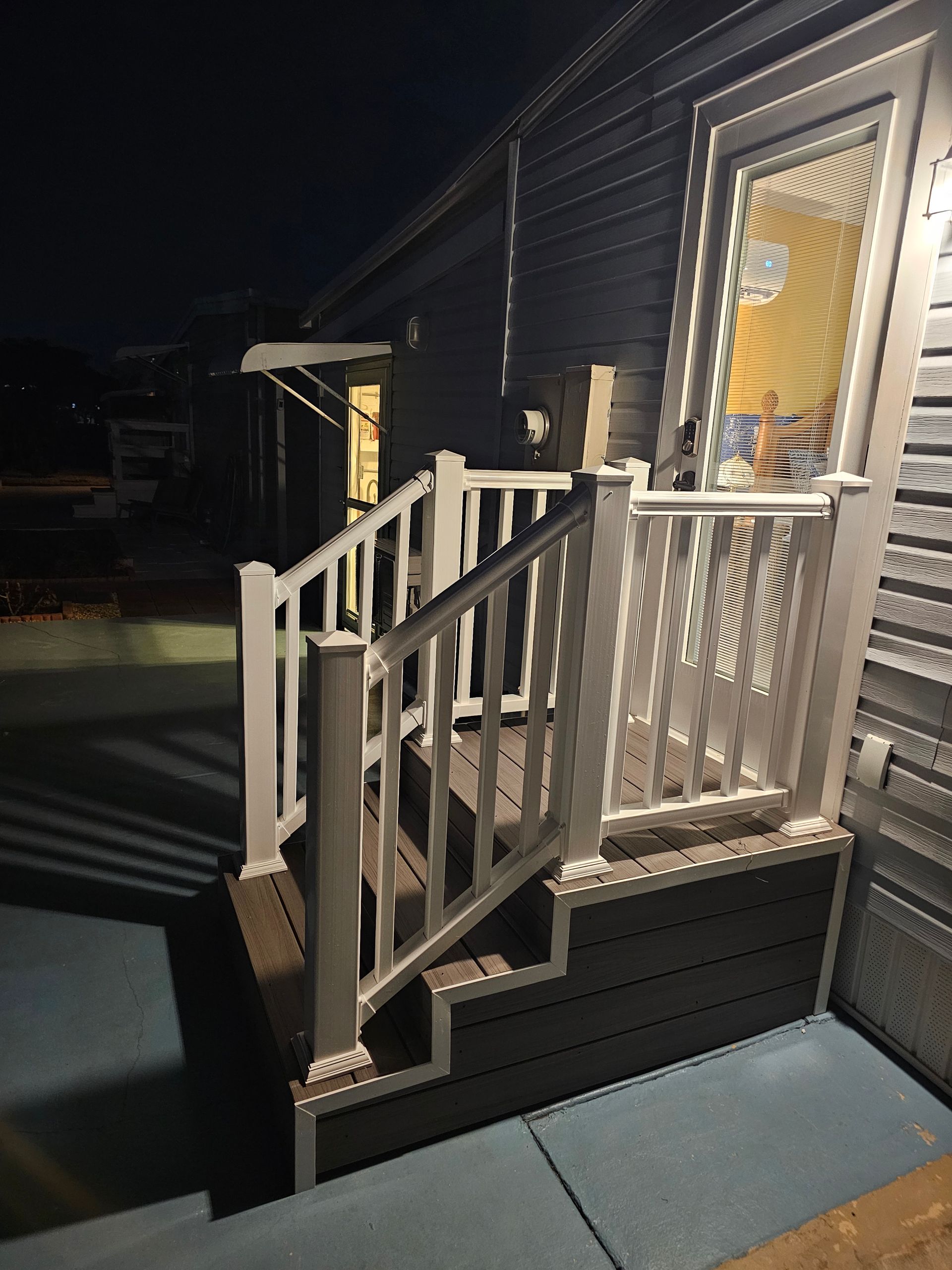 Exterior steps with white railing, leading to a door with light shining from inside.